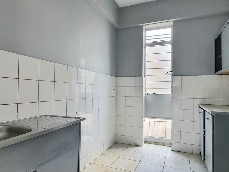 A functional scullery or utility area featuring a stainless steel sink, tiled splashbacks, built-in cabinetry, and a louvered window for ventilation.