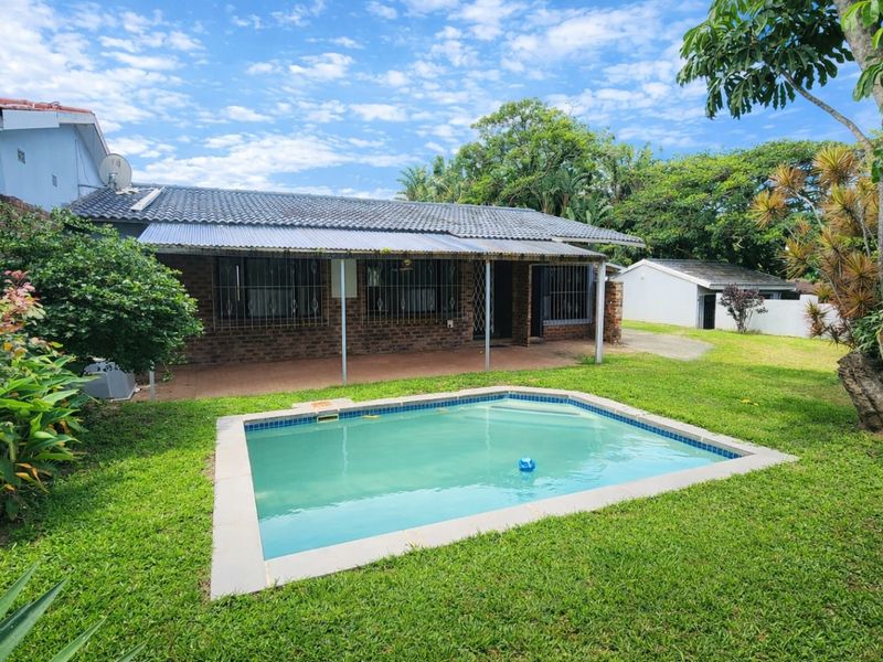 Rear view of the townhouse featuring a private swimming pool, a covered patio area, and a spacious garden with established landscaping.