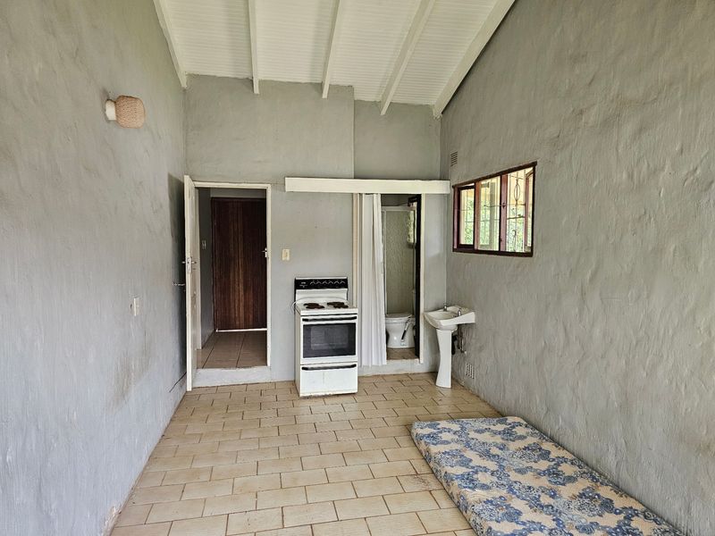 A basic kitchen area featuring tiled flooring, a freestanding stove, and a pedestal basin, with exposed beam ceilings and a simple layout.