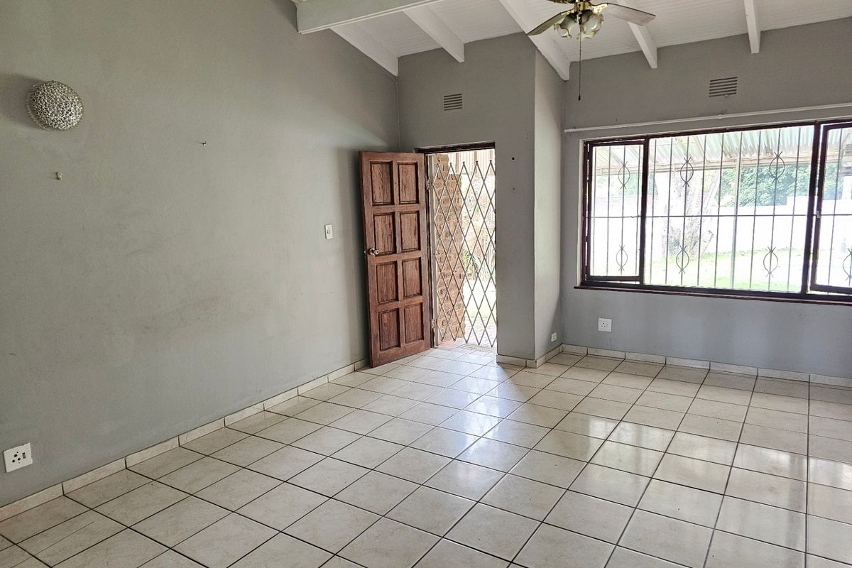 Spacious living area featuring tiled flooring, exposed beam ceilings, and direct access to the exterior through a secure door.