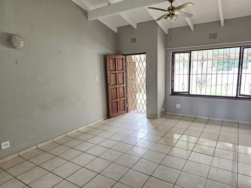 Spacious living area featuring tiled flooring, exposed beam ceilings, and direct access to the exterior through a secure door.