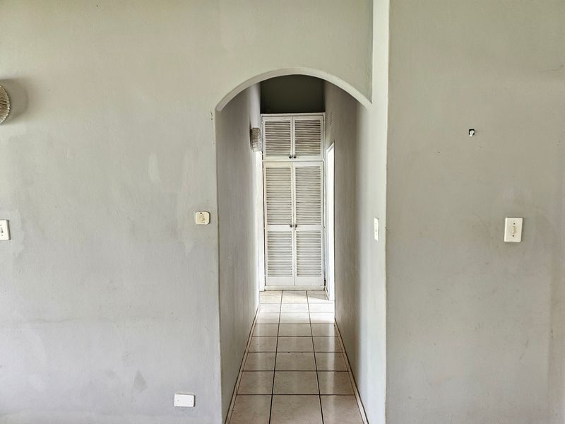 A narrow hallway featuring an arched entrance, tiled flooring, and built-in louvered storage cupboards at the end.