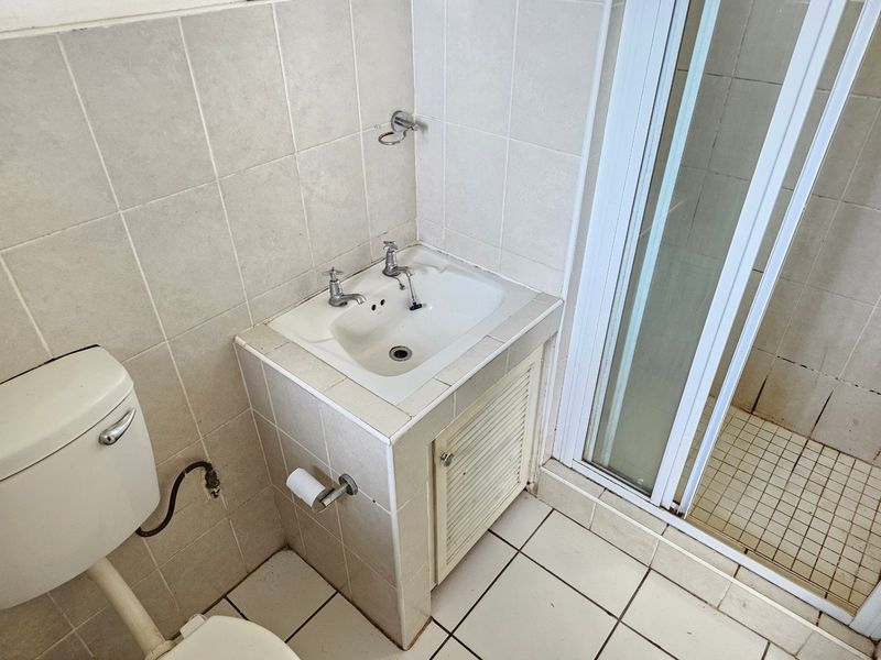 A functional bathroom featuring a tiled vanity with a built-in basin, a shower enclosure, and a standard toilet, requiring cosmetic updates.