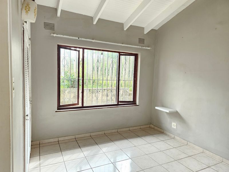 An empty bedroom featuring tiled flooring, exposed beam ceilings, and a window with security bars, offering a blank canvas for potential updates.