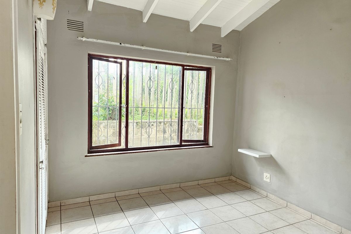 An empty bedroom featuring tiled flooring, exposed beam ceilings, and a window with security bars, offering a blank canvas for potential updates.
