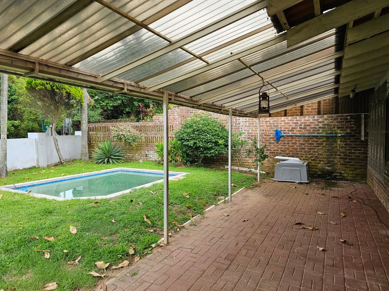 Covered patio area featuring brick paving, overlooking a private swimming pool and garden with established boundary walls.
