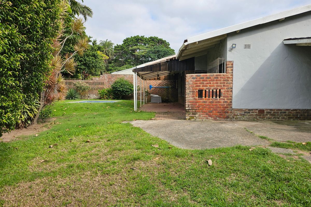 Rear exterior view of the townhouse featuring a lawn, a small swimming pool, a covered patio area, and brick boundary walls.