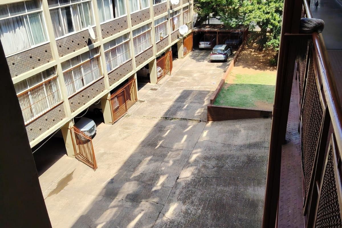 View of the apartment complex rear courtyard featuring a concrete driveway, covered parking bays, and a small garden area.