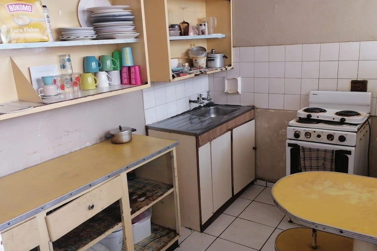 A dated kitchen featuring original cabinetry, a stainless steel sink, tiled backsplash, and a freestanding stove, requiring modernization and cosmetic updates.