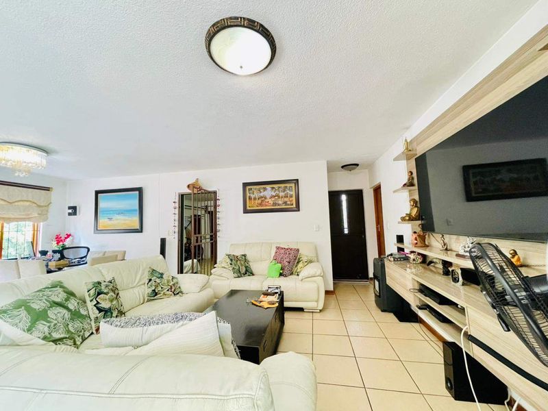 A spacious living room featuring tiled flooring, a built-in media unit, and direct access to the home entrance.
