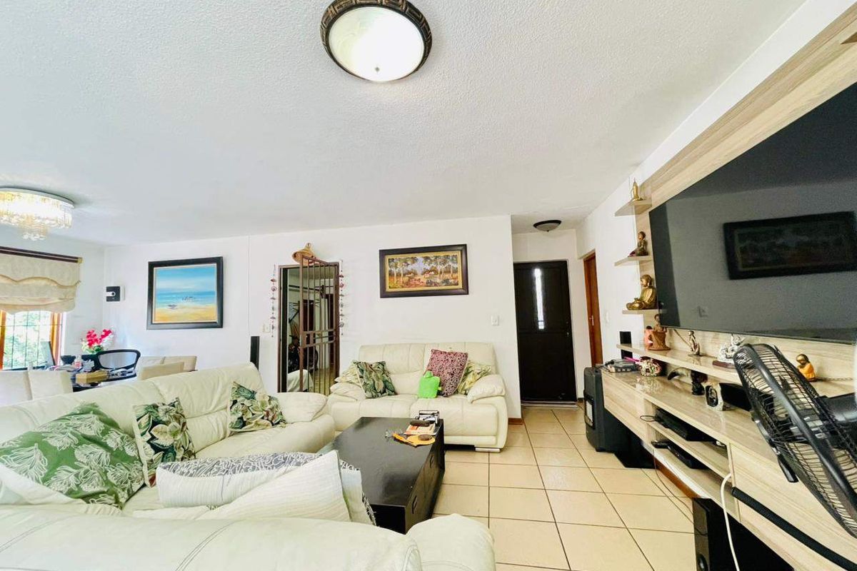 A spacious living room featuring tiled flooring, a built-in media unit, and direct access to the home entrance.