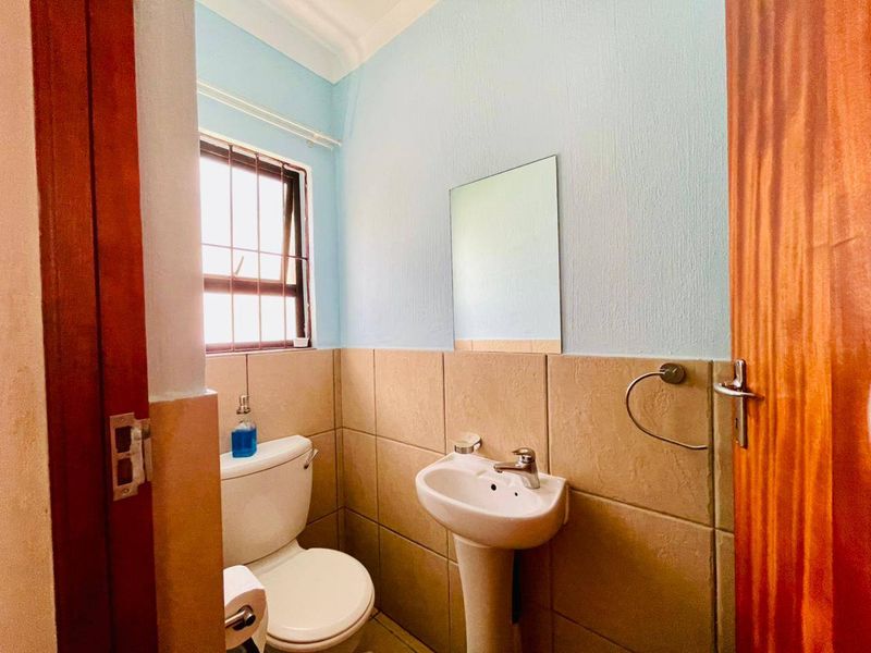 A compact bathroom featuring a pedestal basin, toilet, and tiled splashback, finished with light blue walls and a window with security bars.