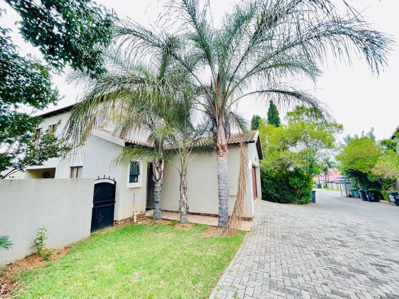 Front exterior view of the townhouse featuring a paved driveway, pedestrian gate, and established palm trees in the front garden area.