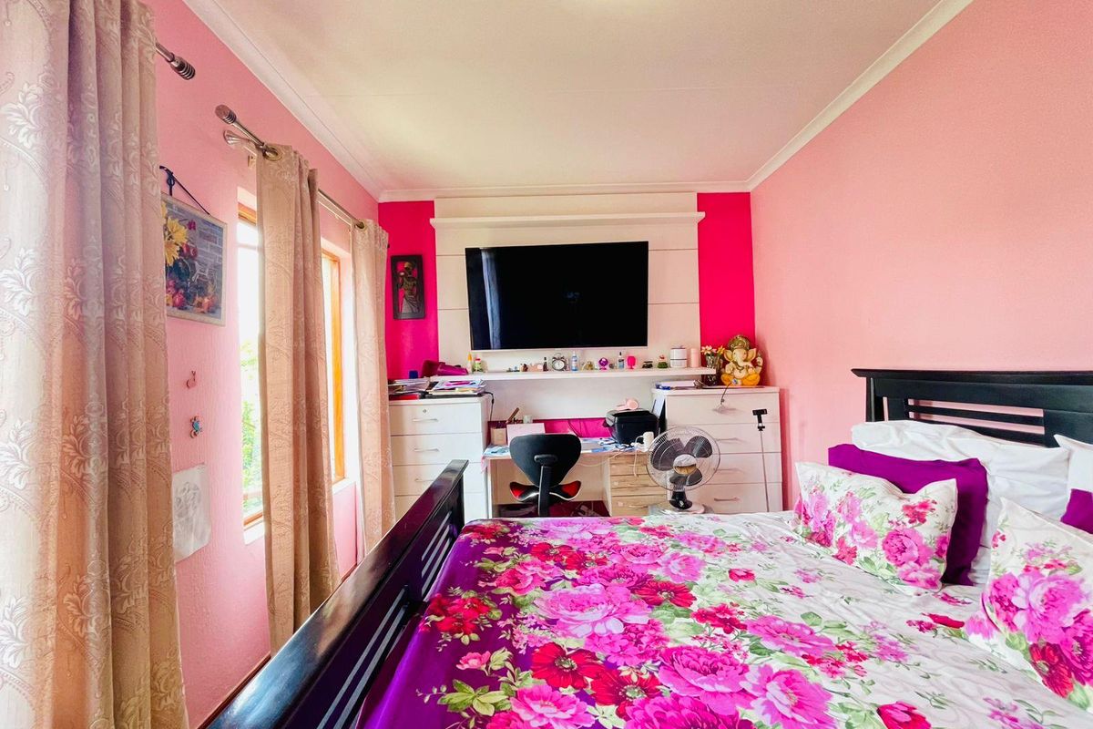 A bedroom featuring a built-in desk and shelving unit, with pink wall finishes and natural light from the side window.