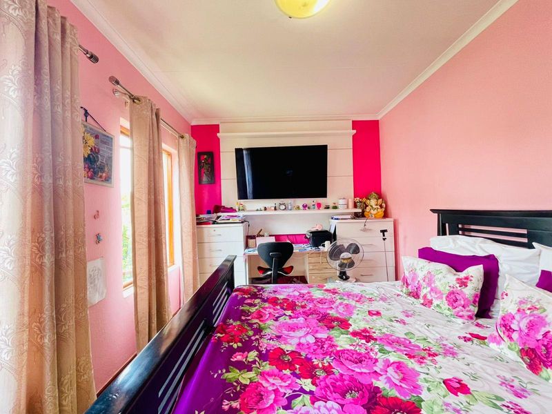 A bedroom featuring a built-in desk and shelving unit, with pink wall finishes and natural light from the side window.