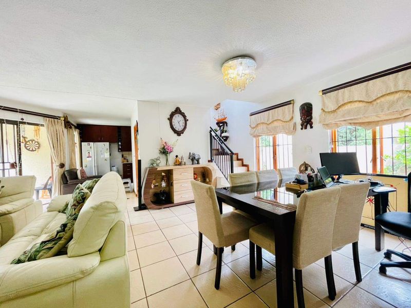Open plan living and dining area featuring ceramic floor tiles, a central staircase, and access to the kitchen and outdoor patio.