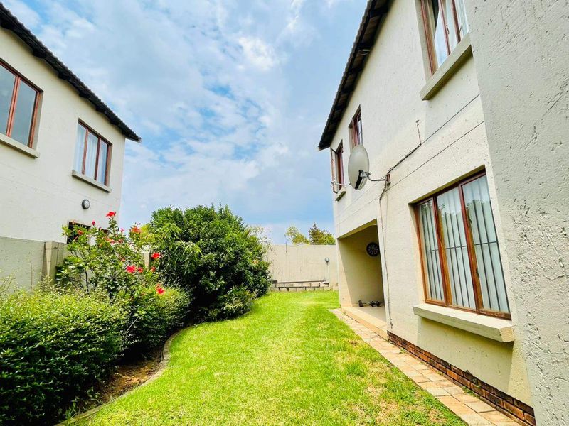 Rear exterior view of the townhouse featuring a private garden, paved walkway, and plastered facade with aluminium window frames.