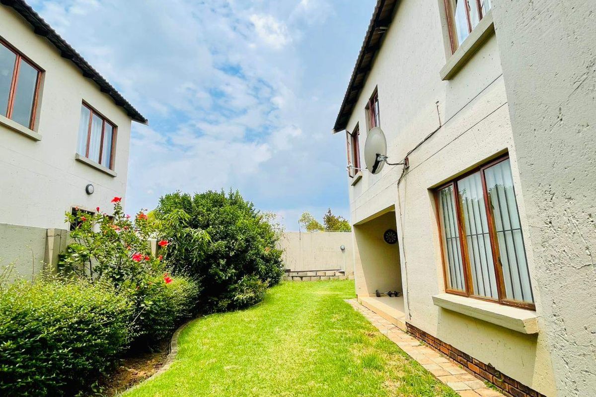 Rear exterior view of the townhouse featuring a private garden, paved walkway, and plastered facade with aluminium window frames.