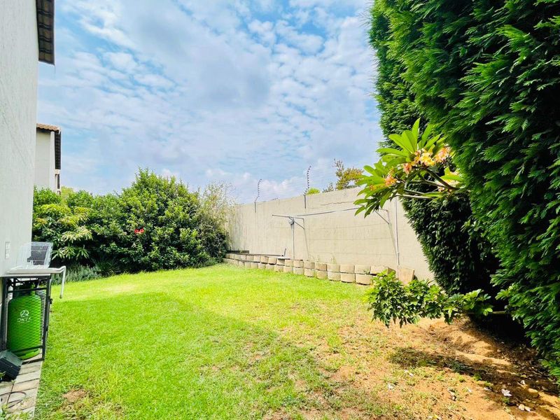 A private rear garden featuring a lawn area, perimeter wall with electric fencing, and established greenery.