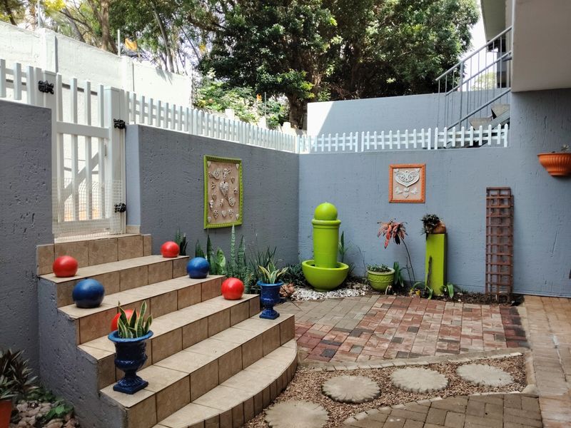 A well-maintained rear courtyard featuring a tiled staircase, paved flooring, and secure boundary walls with a white picket fence.