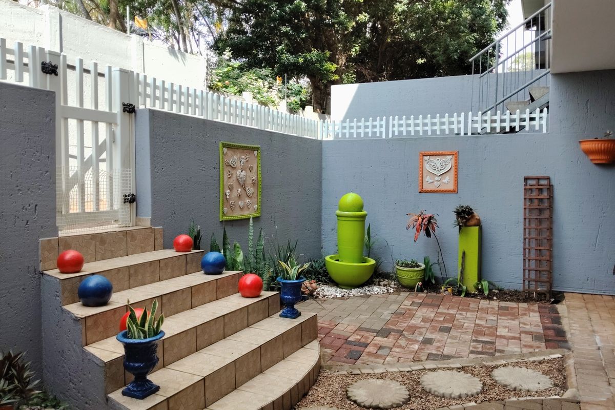 A well-maintained rear courtyard featuring a tiled staircase, paved flooring, and secure boundary walls with a white picket fence.
