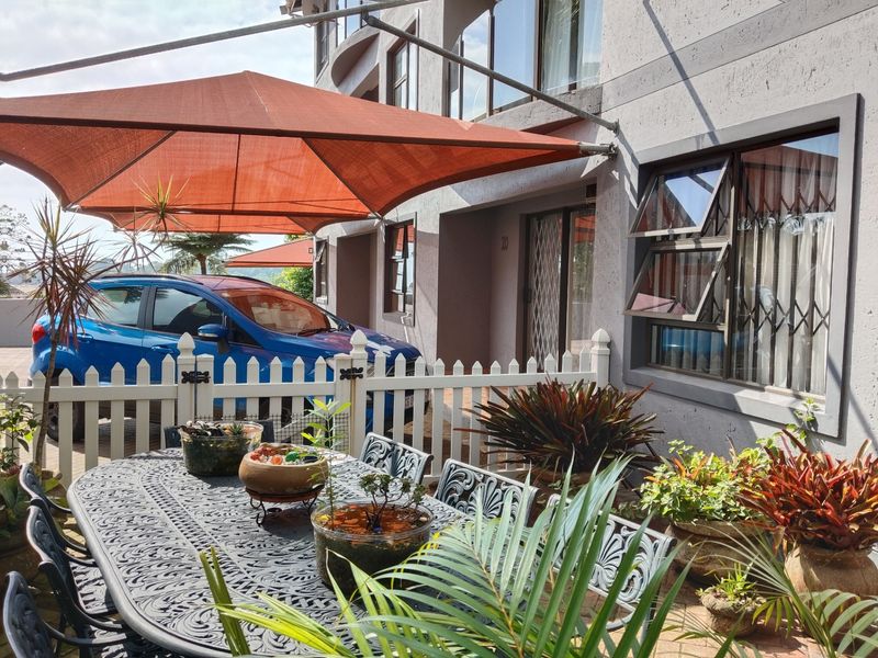 A paved outdoor patio area featuring a shade sail, security gate, and top-hung windows, providing a functional space for outdoor relaxation.