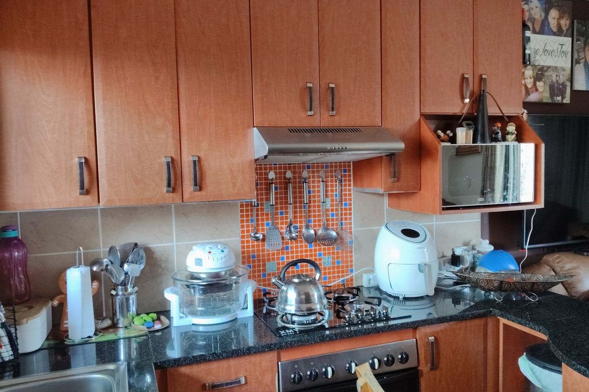 A functional kitchen featuring wood-finish cabinetry, granite countertops, a gas hob with extractor fan, and a vibrant mosaic tile backsplash.