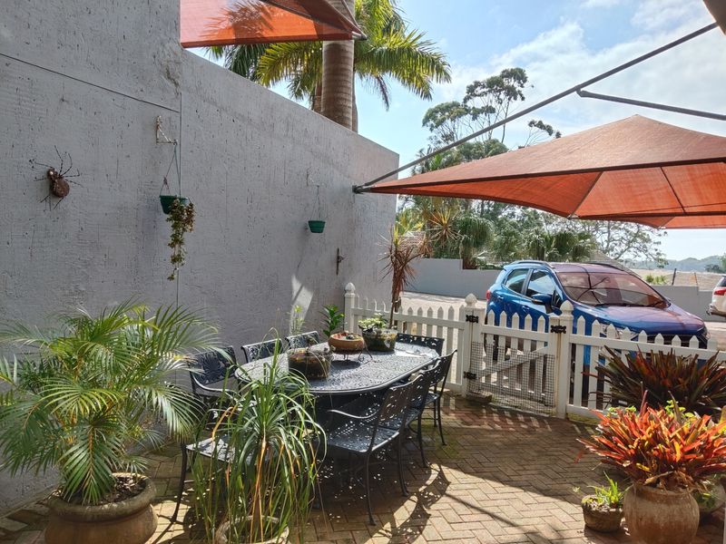 A paved outdoor patio area featuring a white picket fence and a shade sail, providing a functional space for outdoor relaxation.