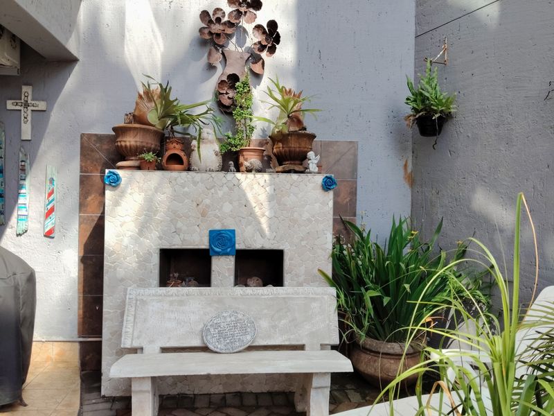 A small outdoor patio area featuring a built-in fireplace with decorative stone cladding and paved flooring, suitable for a cozy seating arrangement.