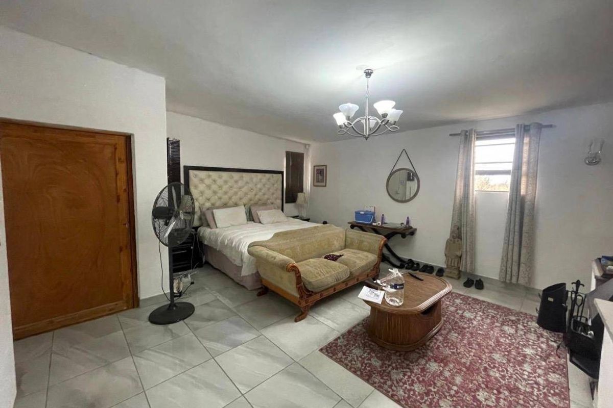 Spacious bedroom featuring tiled flooring, a central chandelier, and a wooden door, offering a functional layout with ample space for furniture.