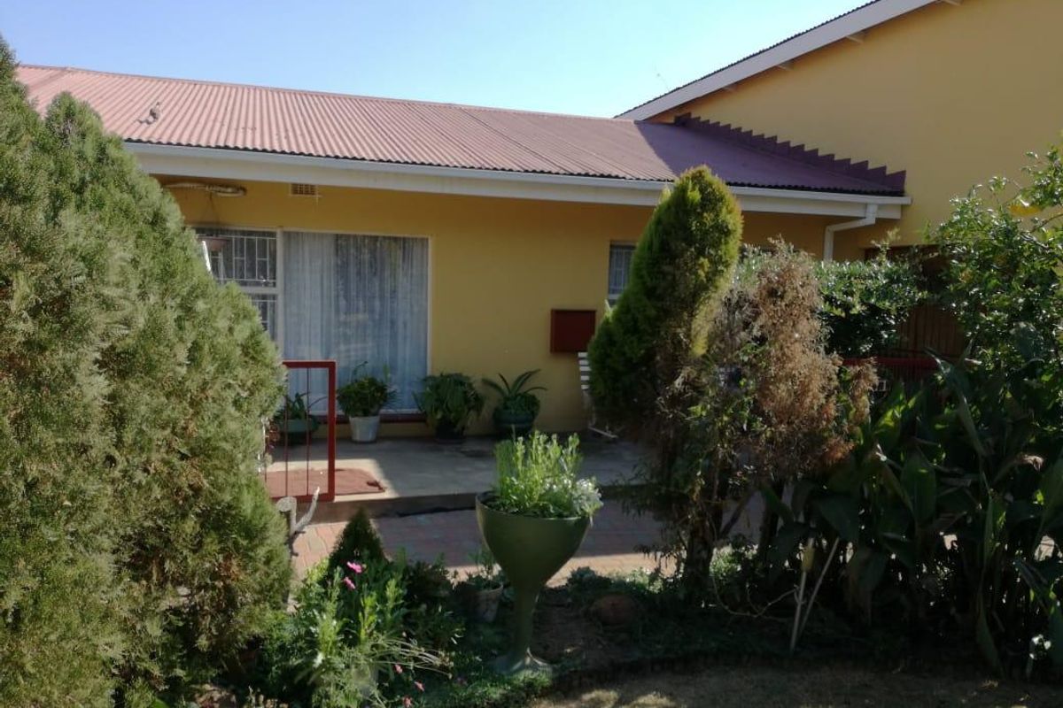 A view of the rear exterior of the house featuring a covered patio area, paved flooring, and established garden landscaping.