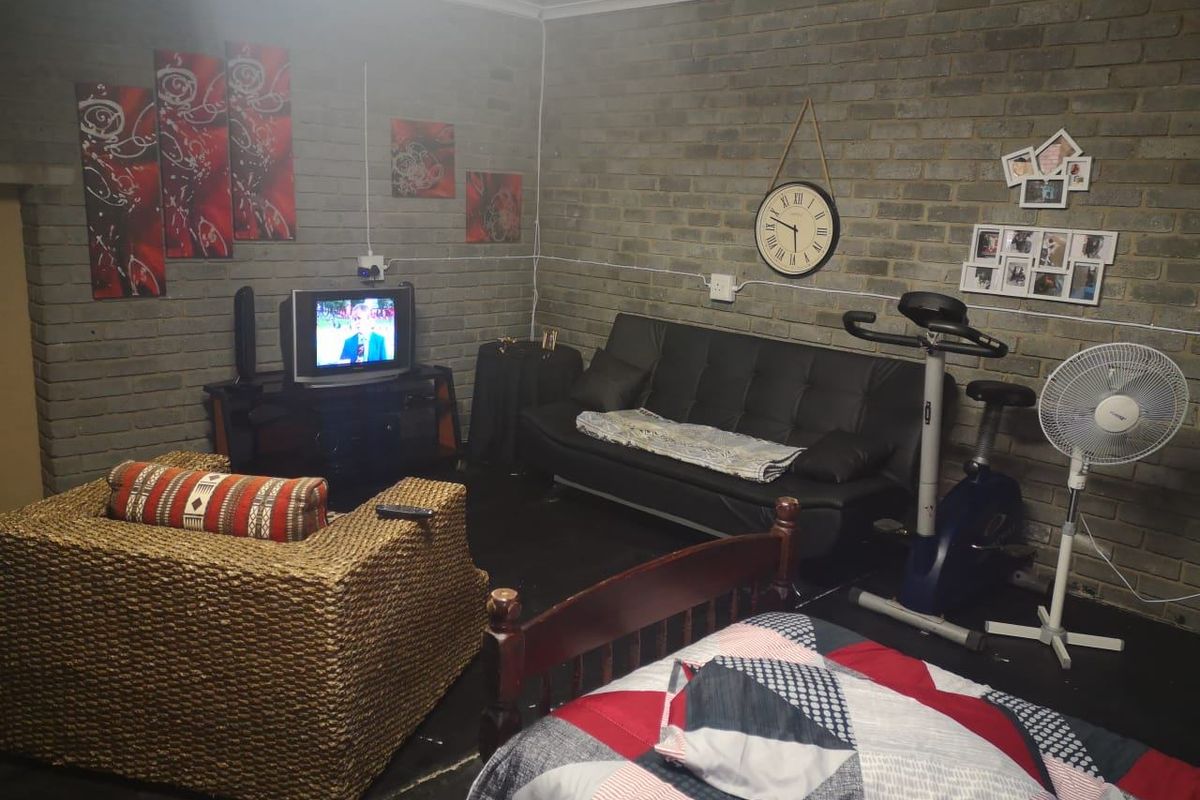 A multi-purpose living and bedroom area featuring exposed brick walls and dark flooring, currently utilized as a combined lounge and sleeping space.