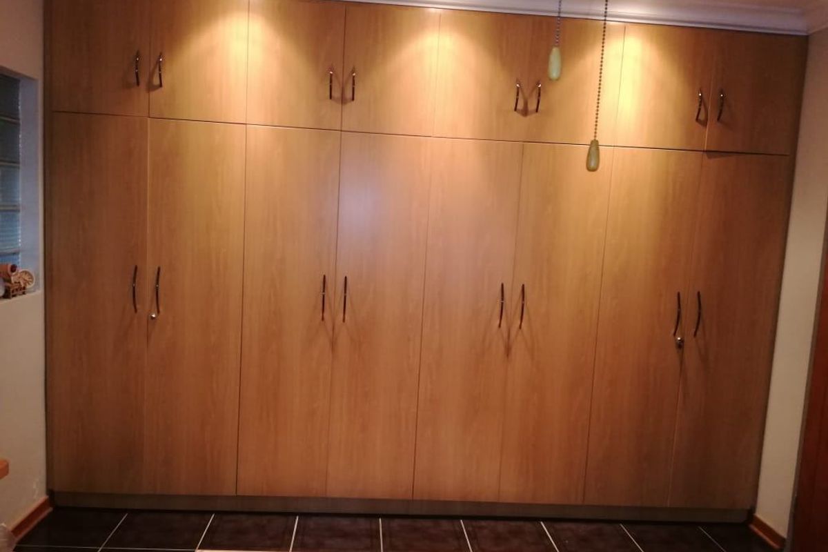 A bedroom featuring extensive floor-to-ceiling built-in wooden cabinetry providing ample storage space, complemented by recessed ceiling lighting and tiled flooring.