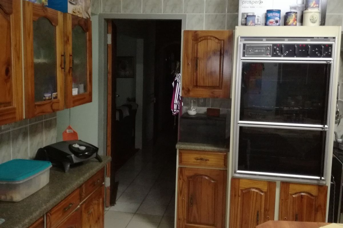 A dated kitchen featuring wooden cabinetry, tiled flooring, and a built-in double oven, offering a functional layout with potential for modernization.