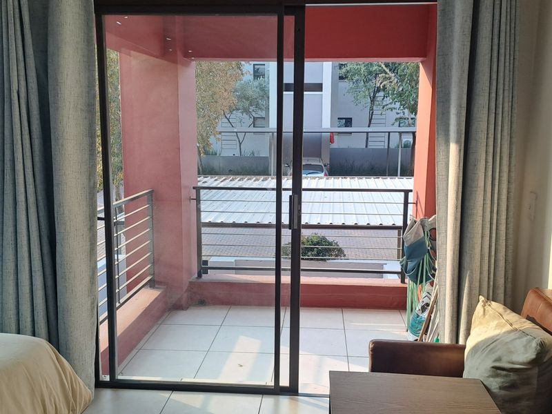 A view from an interior room looking out through a sliding glass door onto a private balcony with metal railings and tiled flooring.