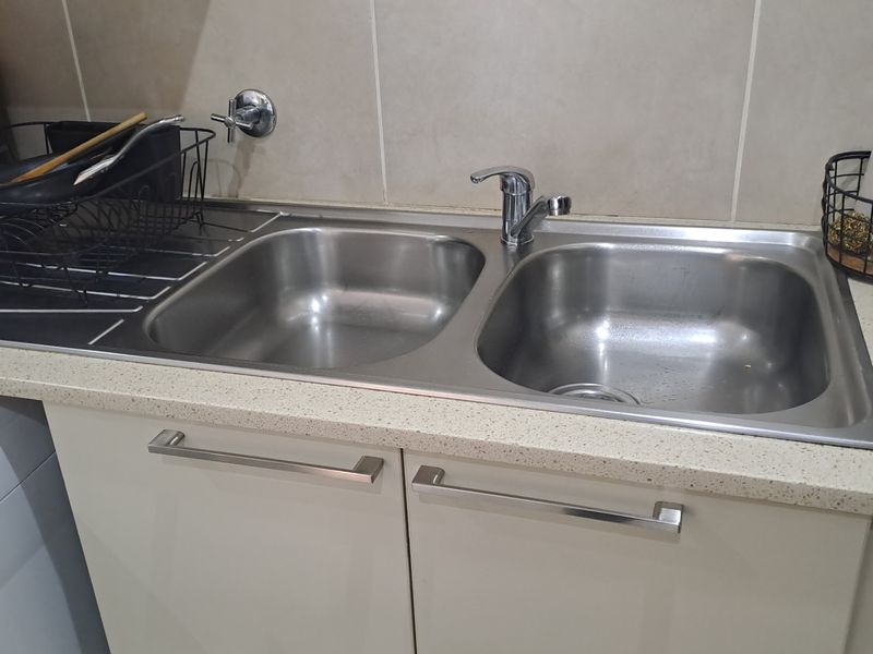 A functional kitchen area featuring a double stainless steel sink with a mixer tap, set into a stone-look countertop with tiled splashback.