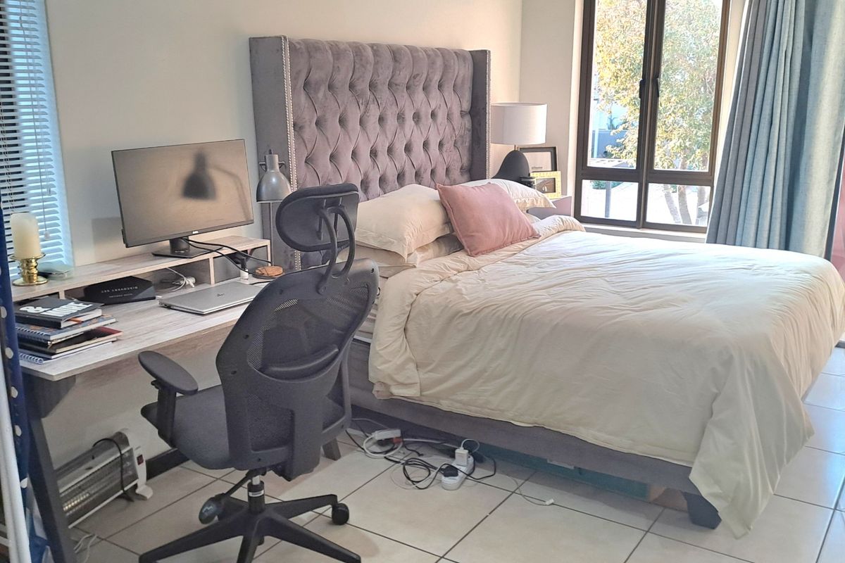 A well-lit bedroom featuring tiled flooring, neutral walls, and large windows with both blinds and curtains, providing a comfortable and functional living space.