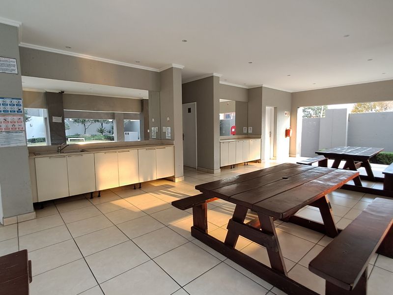 A spacious communal clubhouse area featuring tiled flooring, built-in cabinetry with a sink, and recessed lighting, suitable for social gatherings and events.