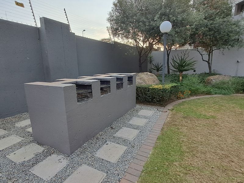 A well-maintained garden area featuring a built-in braai, paved pathways, and secure perimeter walling with electric fencing.