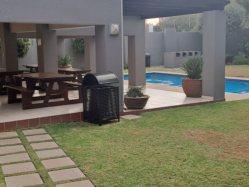 Outdoor entertainment area featuring a covered patio with tiled flooring, a built-in braai, and a swimming pool set within a landscaped garden.