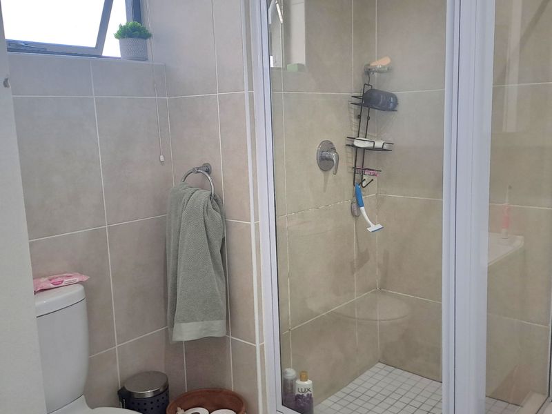 A functional bathroom featuring a glass-enclosed shower, a standard toilet, and neutral wall and floor tiling.