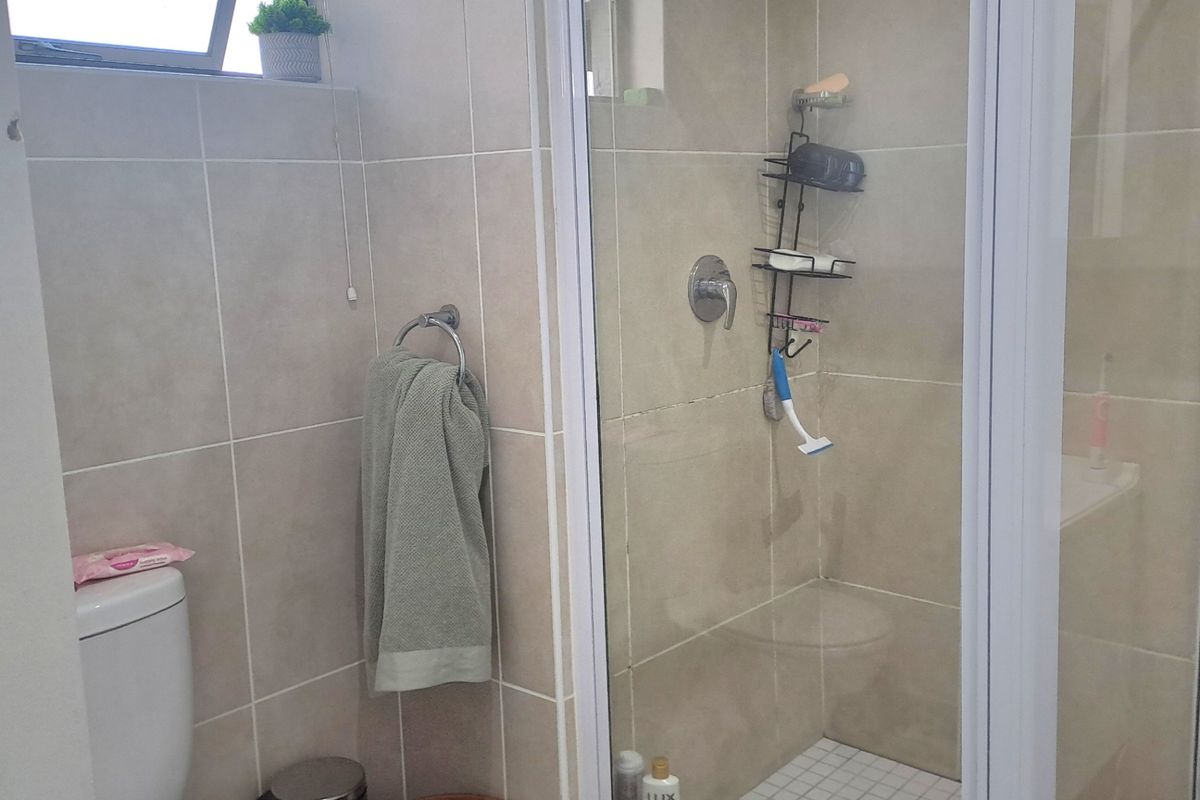 A functional bathroom featuring a glass-enclosed shower, a standard toilet, and neutral wall and floor tiling.