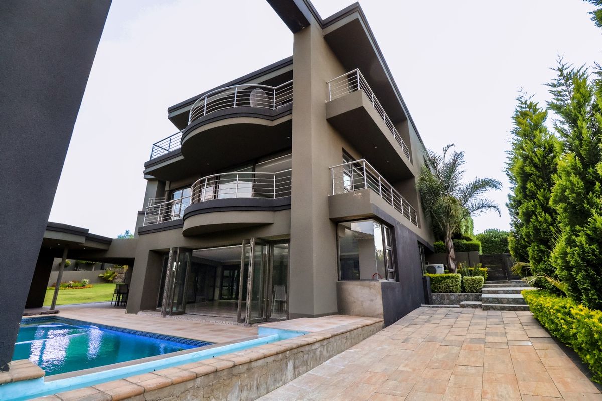 A multi-story modern residence featuring tiered balconies with stainless steel railings, a swimming pool, and expansive stacking doors leading to the patio area.