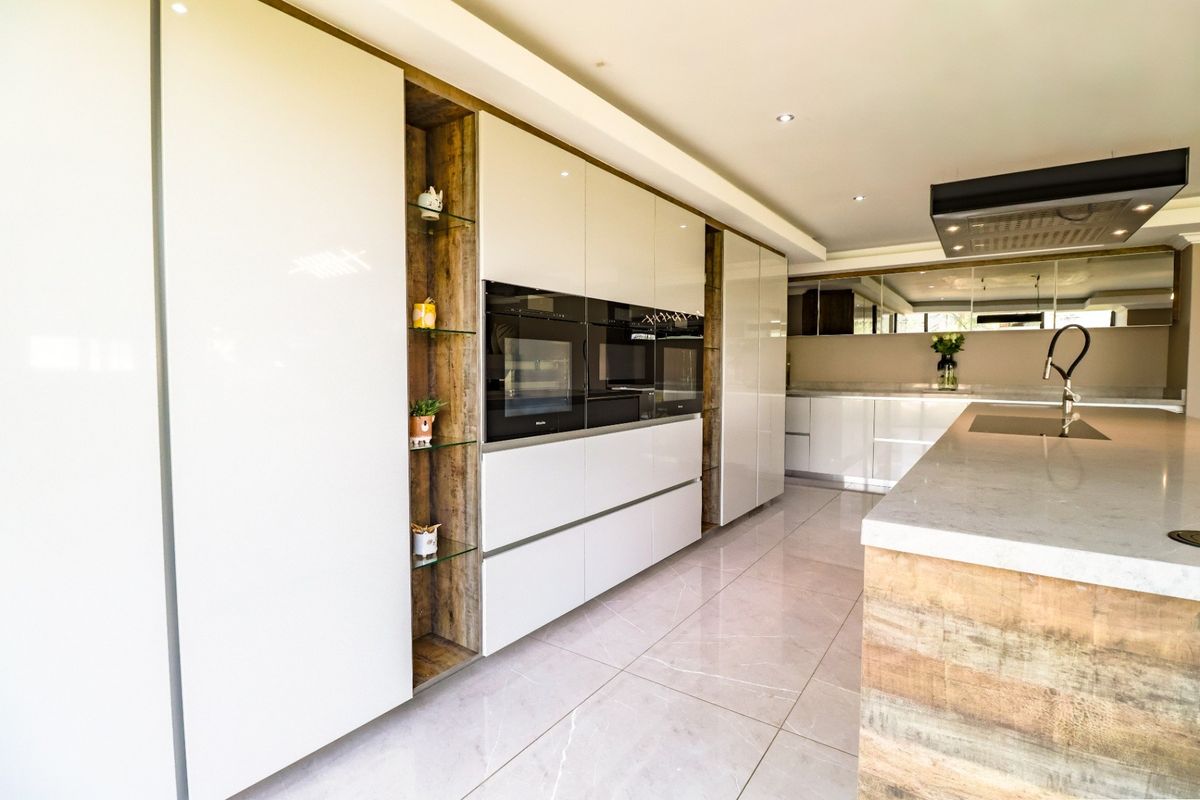 Modern kitchen featuring high-gloss cabinetry, integrated appliances, a large island with stone countertops, and sleek tiled flooring.