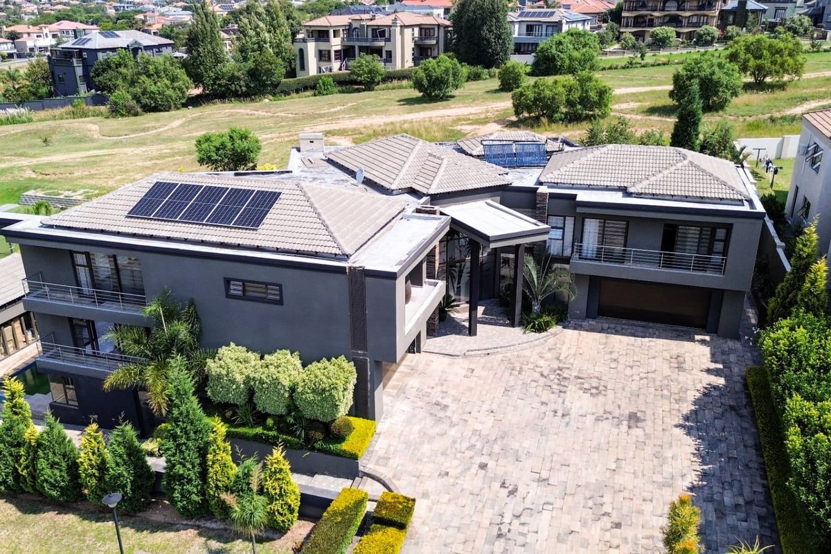 Aerial view of a modern multi-story residence featuring a paved driveway, solar panels, tiled roof, and well-maintained landscaped garden surroundings.