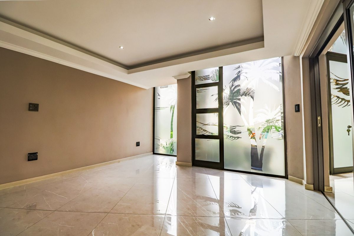 A bright, empty living area featuring polished tiled floors, recessed ceiling lighting, and large frosted glass sliding doors with decorative palm tree patterns.