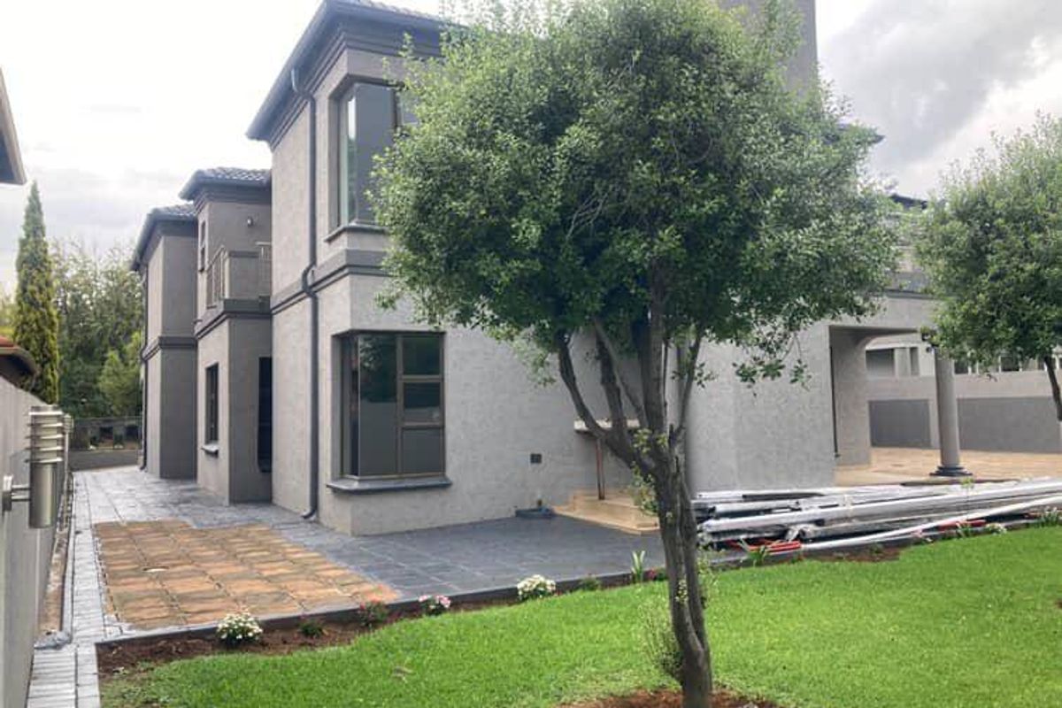 Rear view of a modern two-story house featuring a tiled patio, landscaped garden, paved walkways, and balcony access.
