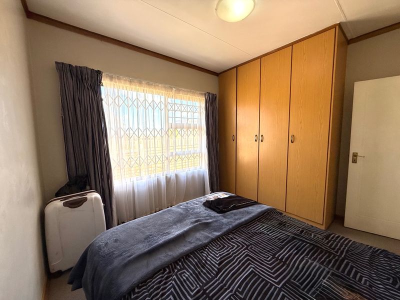A functional bedroom featuring a large built-in wooden wardrobe and a window fitted with a security gate.