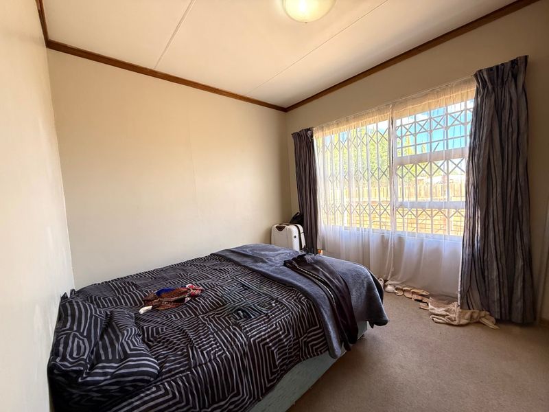 A standard bedroom featuring carpeted flooring, a window with a security gate, and neutral wall finishes.