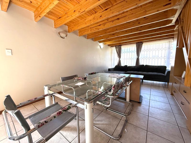 Open-plan living and dining area featuring exposed timber beam ceilings, ceramic tiled flooring, and large windows with security gates.